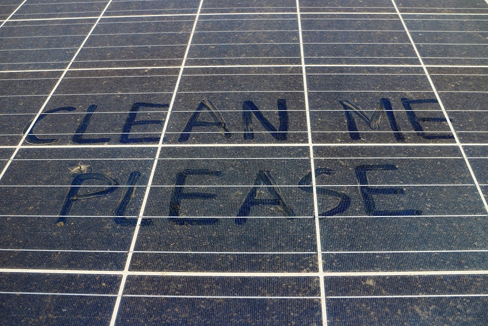 Extremely dirty solar panels with the words Clean Me Please written in the dirt